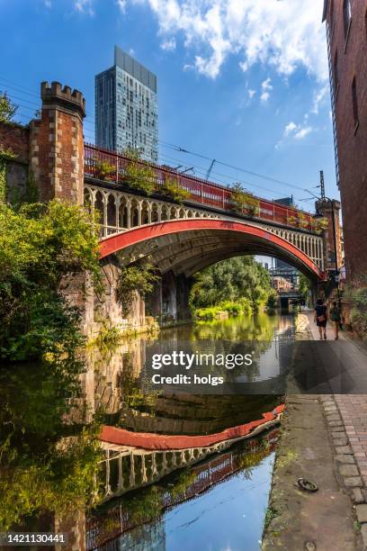 manchester united kingdom railway bridge over a canal in the deansgate area. pedestrians can be seen walking on the towpath - manchester grande manchester imagens e fotografias de stock