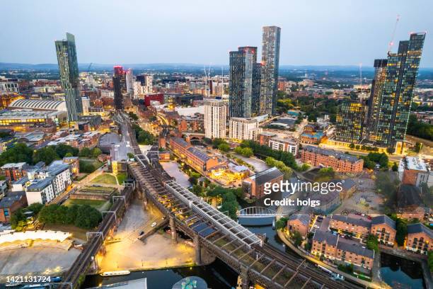 manchester united kingdom aerial shot of modern buildings with lots of counstruction in the central area of the city with historic canals and railways in the foreground by night - manchester england stock pictures, royalty-free photos & images