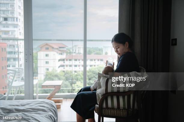 mother feeding baby with milk bottle on armchair in the bedroom. - giving a girl head fotografías e imágenes de stock