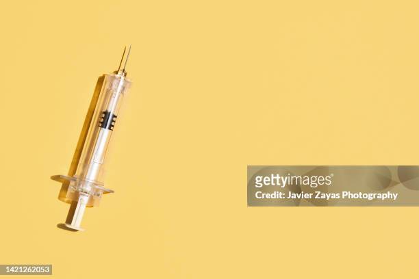 syringe on yellow background - injection stock-fotos und bilder
