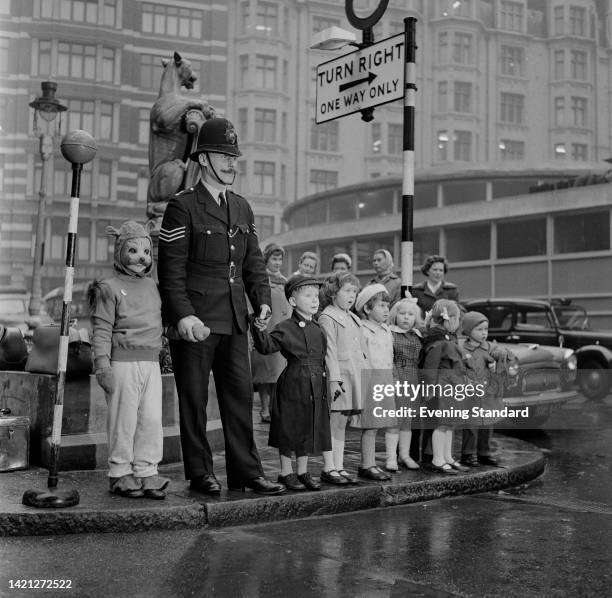 Police officer with a group of children, holding the hand of one child who wears a squirrel mask, during a road safety lesson for the Tufty Club,...