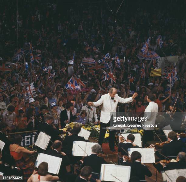 British conductor Norman Del Mar wearing a white tuxedo and black bow tie, his arms outstretched as he conducts the Last Night of the Proms, the...