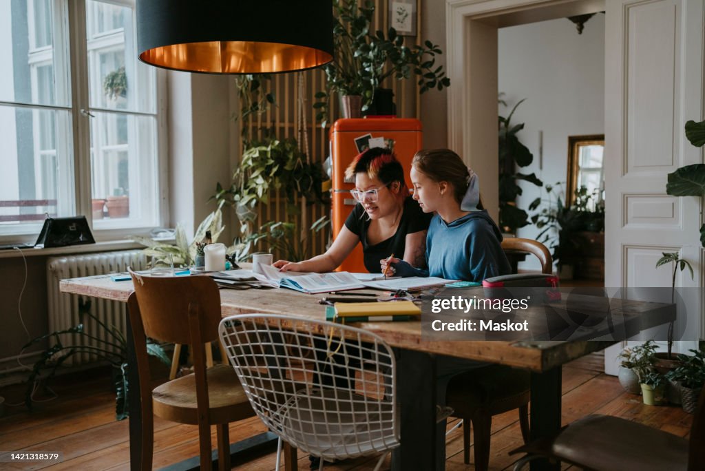 Lesbian mother teaching daughter while sitting at table during studying at home