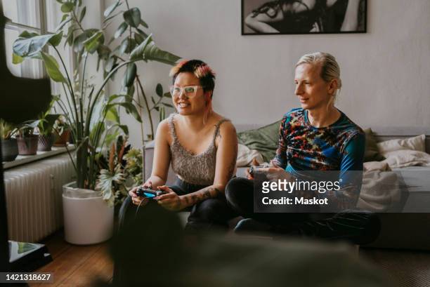 excited gay couple playing video game sitting at home - video game stock-fotos und bilder