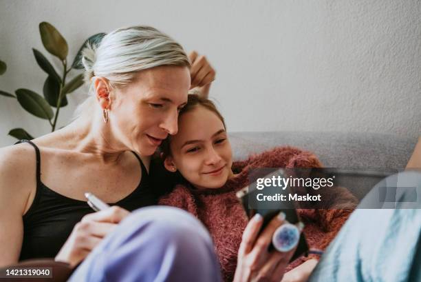 smiling daughter sharing smart phone with mother at home - transgender foto e immagini stock