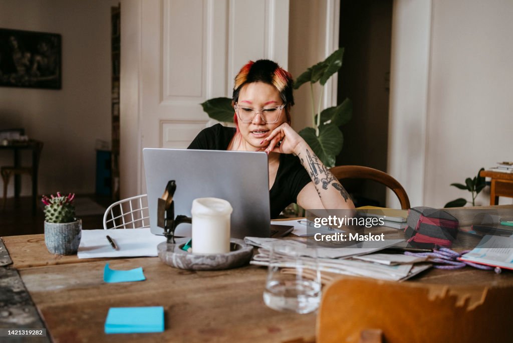 Lesbian freelancer working on laptop while sitting at desk in home