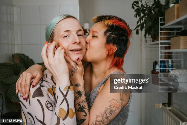 affectionate lesbian woman kissing transgender friend at home - asian lesbians kiss stock pictures, royalty-free photos & images
