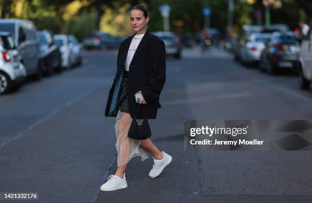 Jana Aasland is seen wearing gold earrings, gold necklace, white t-shirt, black oversize blazer, black short skirt, beige transparent tulle midi...