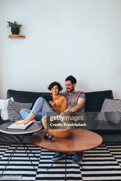 una pareja feliz que se relaja mientras ve algo en las redes sociales usando su tableta - biparental fotografías e imágenes de stock