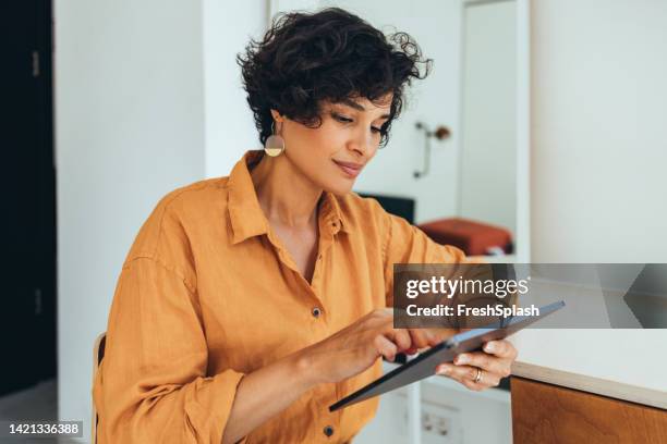 une belle pigiste heureuse lisant quelque chose sur les réseaux sociaux à l’aide de sa tablette - woman with orange photos et images de collection