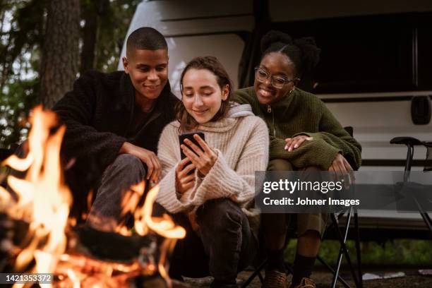 friends sitting by campfire and using phone - in touch with nature stock pictures, royalty-free photos & images