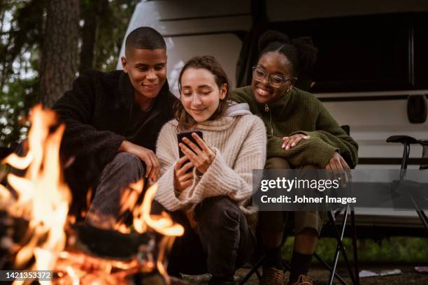 friends sitting by campfire and using phone - ekoturism bildbanksfoton och bilder