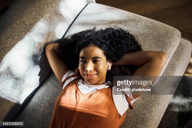 relax woman with earphones listening to podcast or music on sofa with sunshine. gen z black girl or lazy teenager enjoying playlist, audio or songs on wireless technology on a couch on the weekend - hands behind head stock pictures, royalty-free photos & images