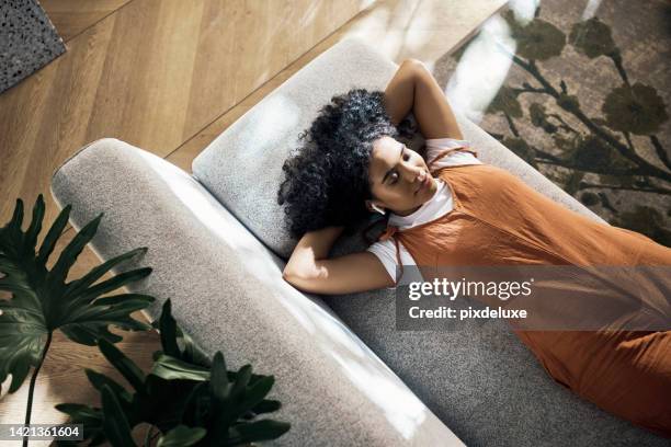 sofa, girl and wireless earphones with music to relax with comfortable lying down position rest. woman streaming soothing app in living room for tranquil and calm chill break time alone. - muziekstreamingdienst stockfoto's en -beelden