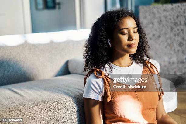 relax, music and meditation of a woman in calm, relaxing and peaceful mind by sofa at home. young black female in stress relief by couch in relaxed body listening to calm audio sounds with earpods - in ear headphones stock pictures, royalty-free photos & images