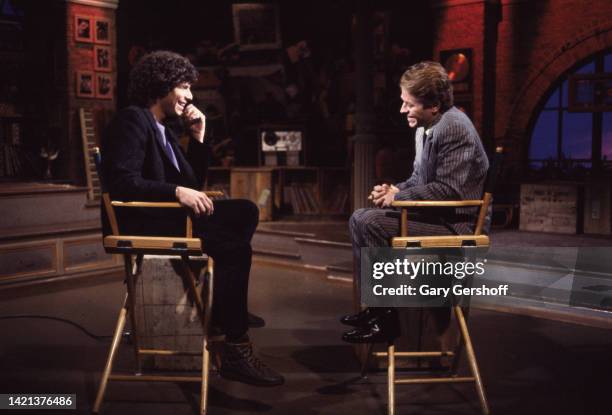View of MTV VJ Mark Goodman and British Pop & Rock musician Robert Palmer as they sit in director's chairs during an interview on MTV at Teletronic...