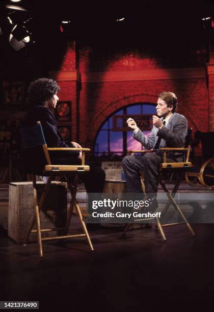 View of MTV VJ Mark Goodman and British Pop & Rock musician Robert Palmer as they sit in director's chairs during an interview on MTV at Teletronic...