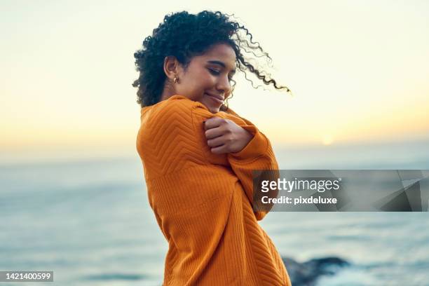 happy black woman embrace herself on a beach at sunrise, self love and peaceful. young african american feeling in touch with earth and nature, enjoy freedom and inner peace, smiling, loving soul - hair love 個照片及圖片檔