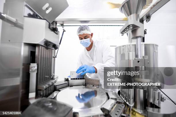 pharmaceutical technician in a protective clothing equipment seen in a laboratory during a manufacturing process - medische apparatuur stockfoto's en -beelden
