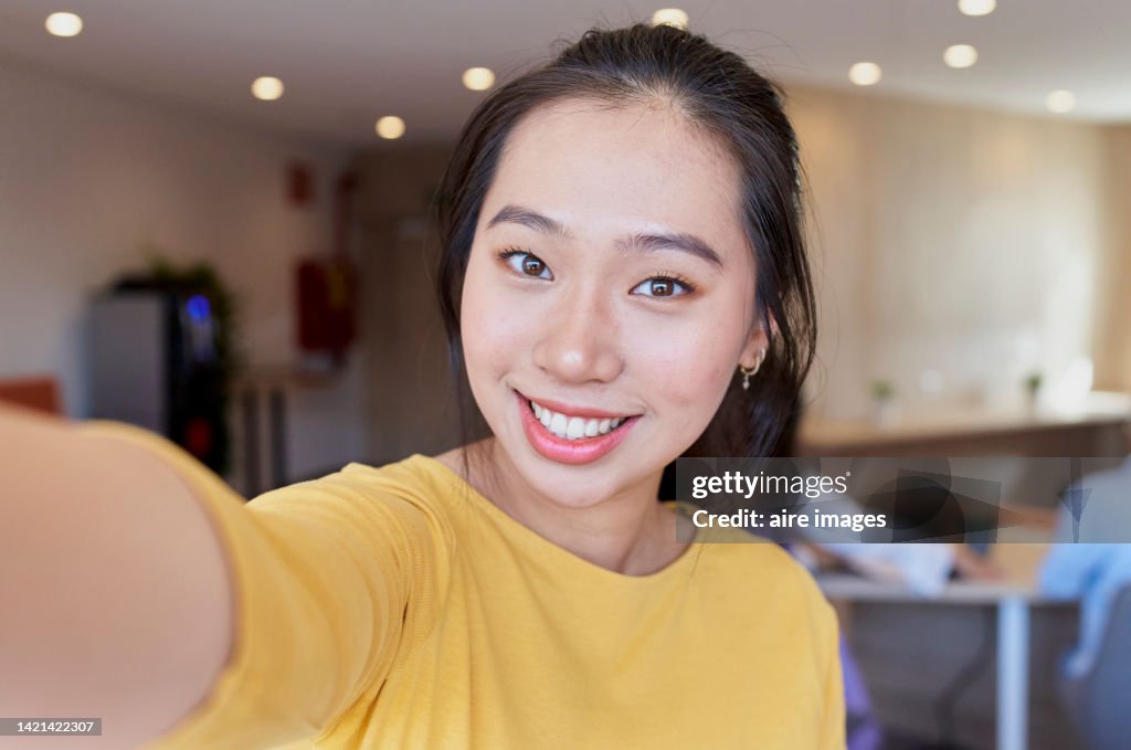 Portrait of young asian woman holding camera and smiling with unfocused background