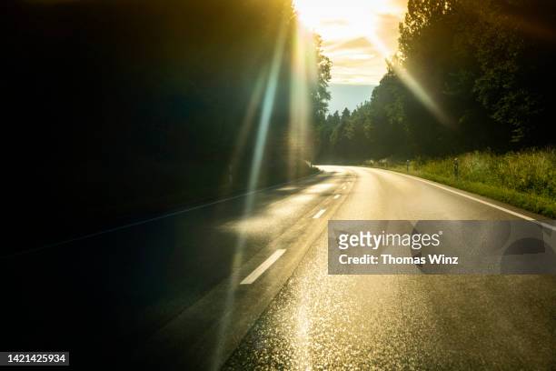 driving on a country road into the sun - country roads stock-fotos und bilder