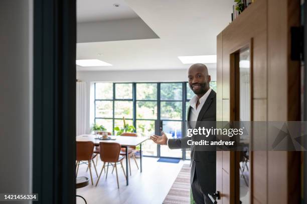 welcoming real estate agent opening the door of a house for sale - abertura imagens e fotografias de stock