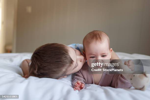 cute siblings lying on the bed at home - newborn sibling stock pictures, royalty-free photos & images