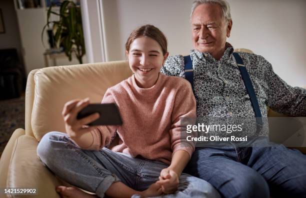 grandfather and happy granddaughter taking selfie at home - modern manlighet bildbanksfoton och bilder