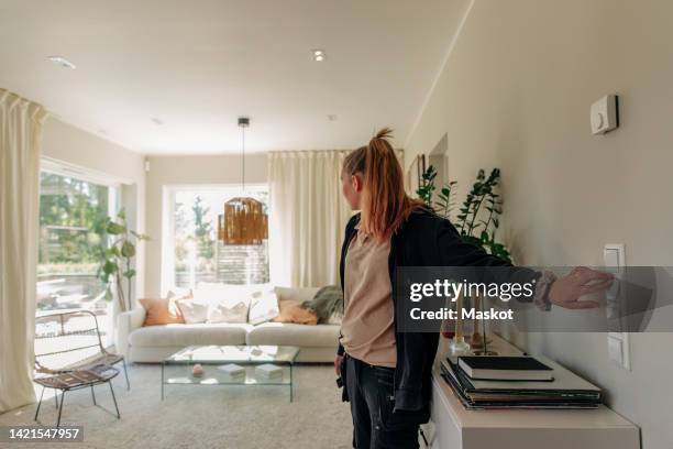 female electrician turning on light switch while checking pendant light in living room - turning on or off stock pictures, royalty-free photos & images