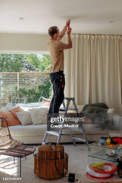 full length side view of technician installing equipment while standing on ladder at home - man standing full length side stock-fotos und bilder