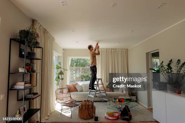 side view of male technician installing electrical equipment on ceiling in living room at home - decoração de quarto rapaz imagens e fotografias de stock