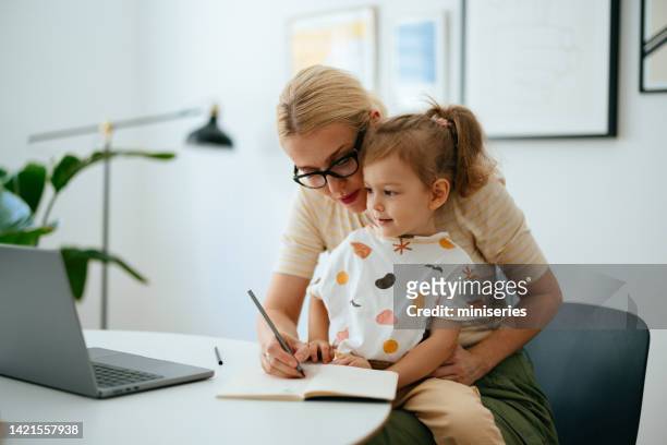 maman qui travaille utilise l’ordinateur portable à la maison tout en prenant soin de sa jeune fille - girl business photos et images de collection