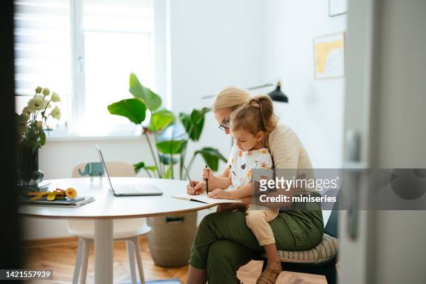 working mom using the laptop at home while taking care of young daughter - babysitter stock pictures, royalty-free photos & images