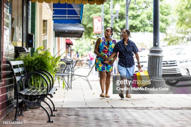 lesbian couple walking through small town shopping district - localidad pequeña fotografías e imágenes de stock
