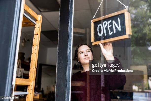 female small business owner turning open sign in her store - abierto fotografías e imágenes de stock