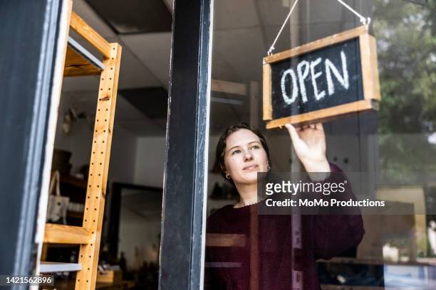 female small business owner turning open sign in her store - bord open stockfoto's en -beelden
