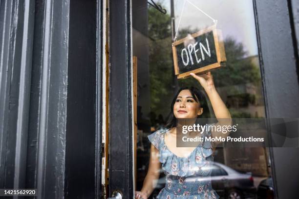 female small business owner turning open sign in her store - klein bedrijf stockfoto's en -beelden