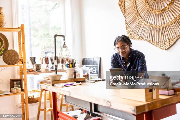 female small business using smartphone in her store - small business stockfoto's en -beelden