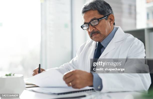 doctor doing medical paperwork in his office at the clinic while sitting and writing at desk. scientist analyzing the hospital patient results. healthcare worker reading medicare insurance documents. - reading document stock pictures, royalty-free photos & images