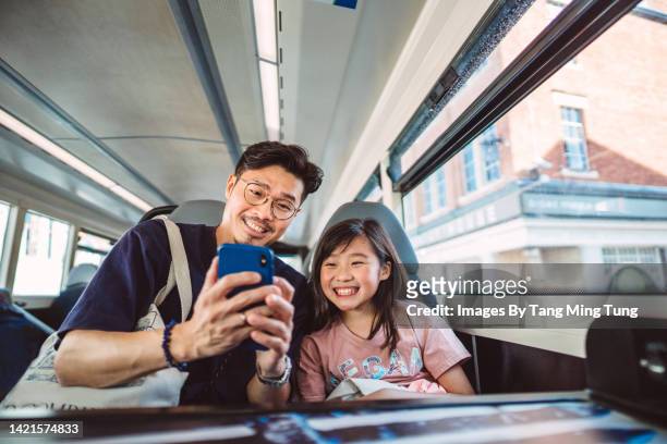 Young handsome dad using smartphone joyfully with his lovely daughter while travelling on bus