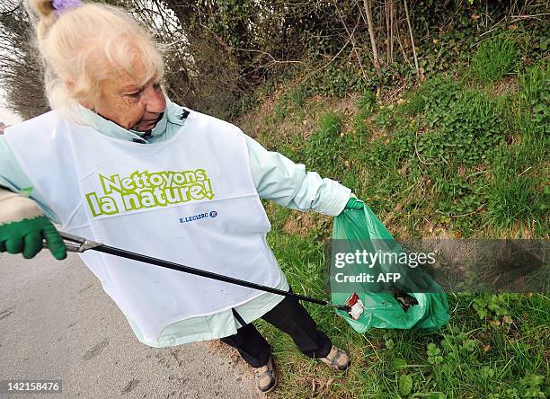 Une personne bénévole participe à une opération "Nettoyons la Nature" en ramassant des détritus dans un fossé sur le bas-côté d'une route à...