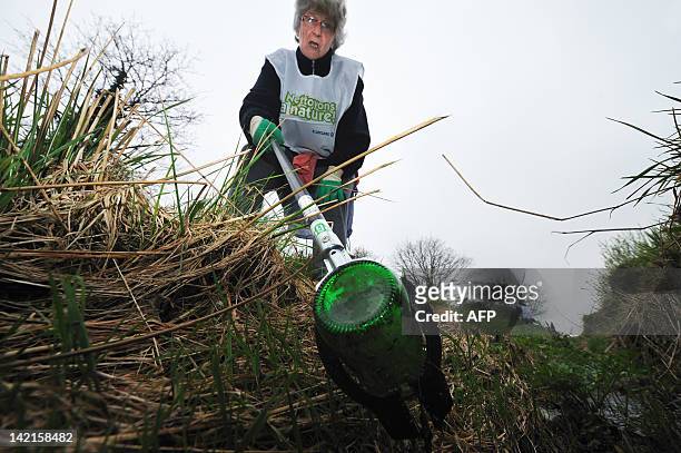 Une personne bénévole participe à une opération "Nettoyons la Nature" en ramassant des détritus dans un fossé sur le bas-côté d'une route à...