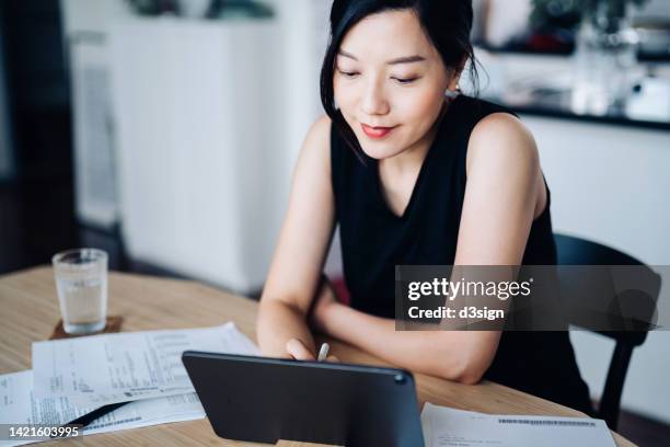 young asian woman handling personal banking and finance with digital tablet at home. planning budget and calculating expenses. managing taxes and financial bills. wealth management. digital banking habits. smart banking with technology - statement stock pictures, royalty-free photos & images