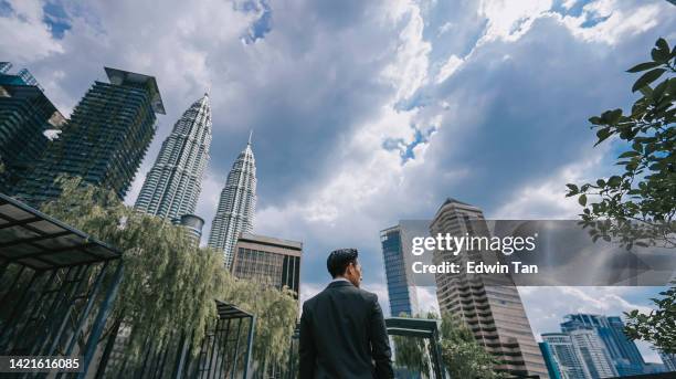 vista traseira empresário chinês asiático parado no telhado jardim edifício de escritórios na cidade durante a manhã olhando para o lado - kuala lumpur - fotografias e filmes do acervo