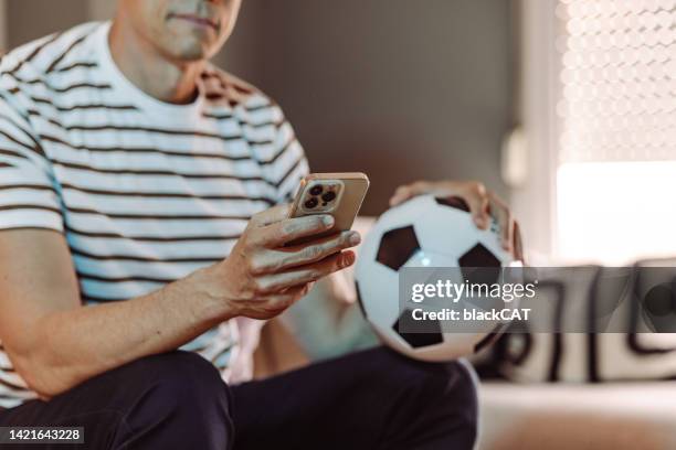cheerful mature man watching a football match at home and checking results on his smart phone - glee tv program stockfoto's en -beelden