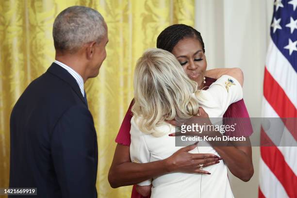 Former U.S. President Barack Obama looks on as former first lady Michelle Obama hugs U.S. First lady Jill Biden during a ceremony to unveil their...