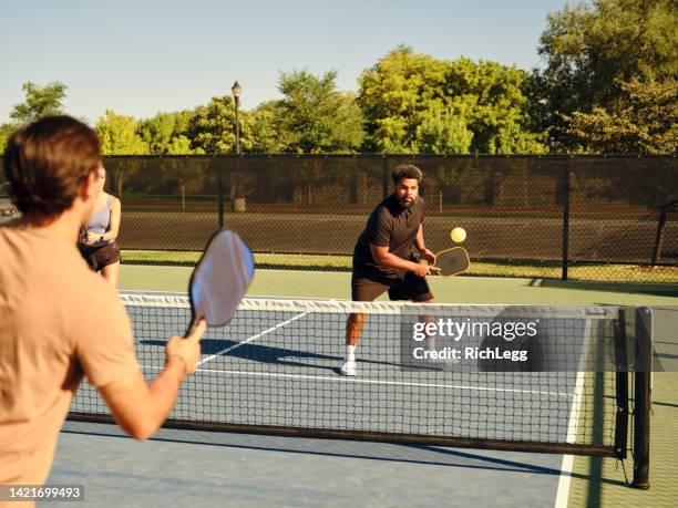 young adults playing pickleball on a public court - paddle tennis stock pictures, royalty-free photos & images