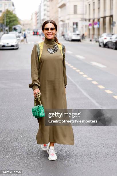 Gitta Saxx, wearing a khaki colored silk dress with shoulder and chest emblems by Marcel Ostertag, sneakers by Puma, a green bag by Zara and...