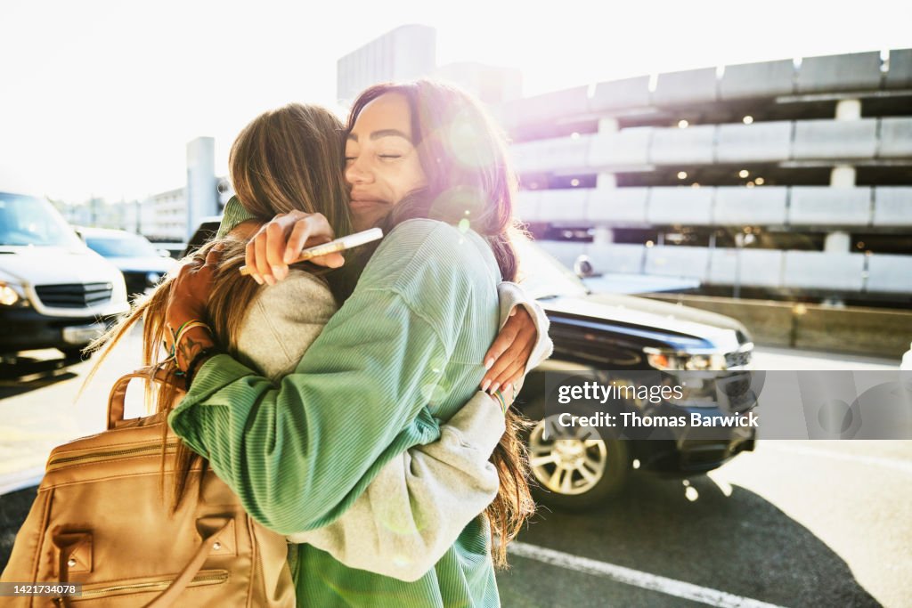 Medium shot of mother and daughter hugging curbside at airport