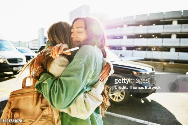 medium shot of mother and daughter hugging curbside at airport - krama bildbanksfoton och bilder